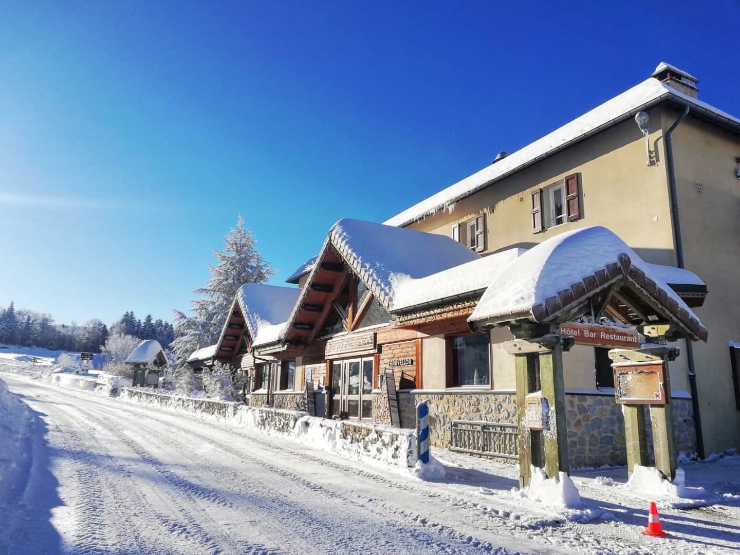 L’auberge et la chaussée sont recouvertes de neige sous un ciel bleu.