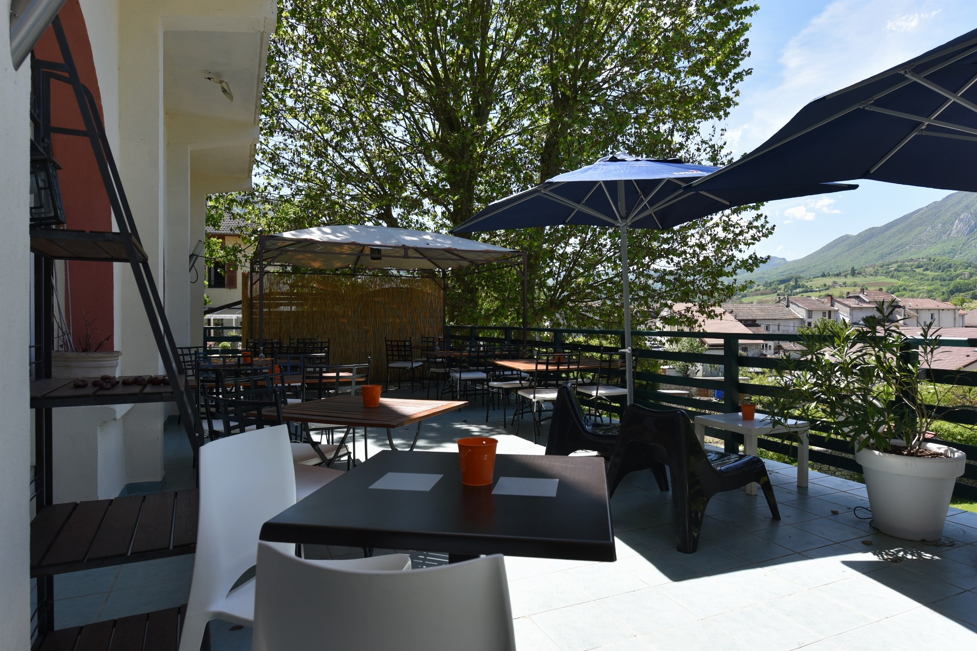 Une pergola et deux grands parasols abritent des tables et des chaises sur une terrasse spacieuse, le tout baigné de soleil et entouré d’une végétation luxuriante