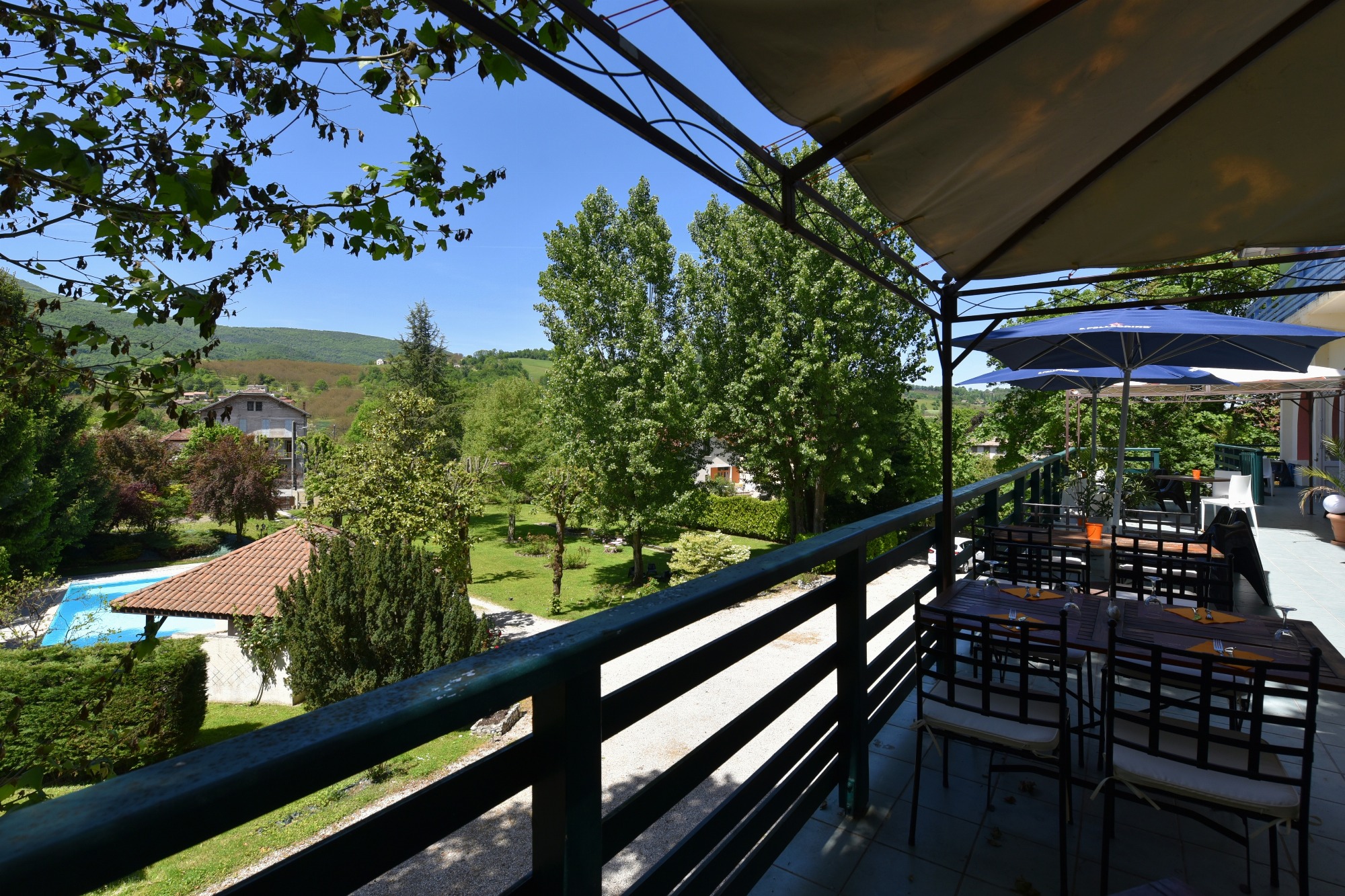 Panorama sur la terrasse, le jardin verdoyant et la piscine sous un ciel lumineux d’été