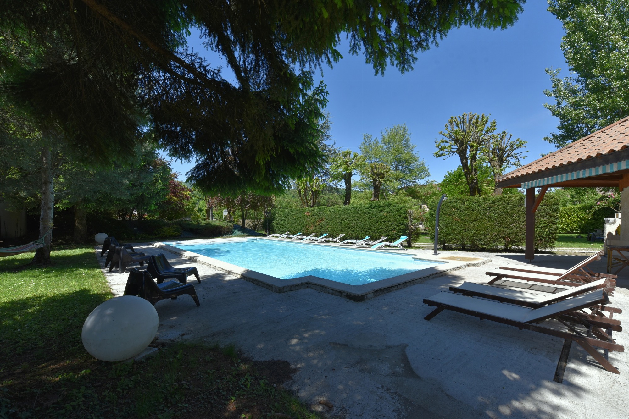 Grande piscine extérieure bordée de sièges et de transats, au cœur d’un cadre verdoyant
