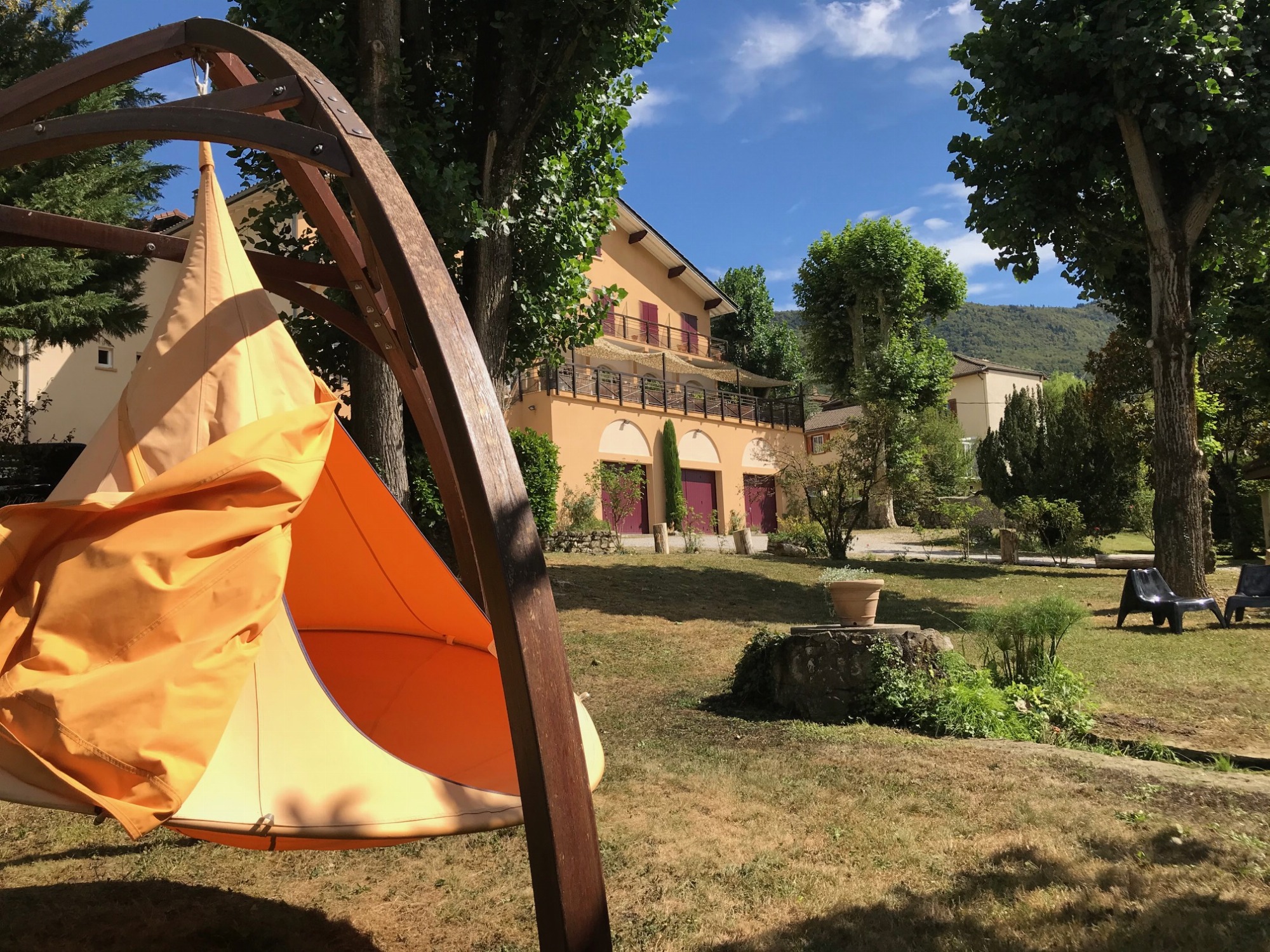 Tipi installé dans un jardin baigné de lumière avec assises et entouré de végétation