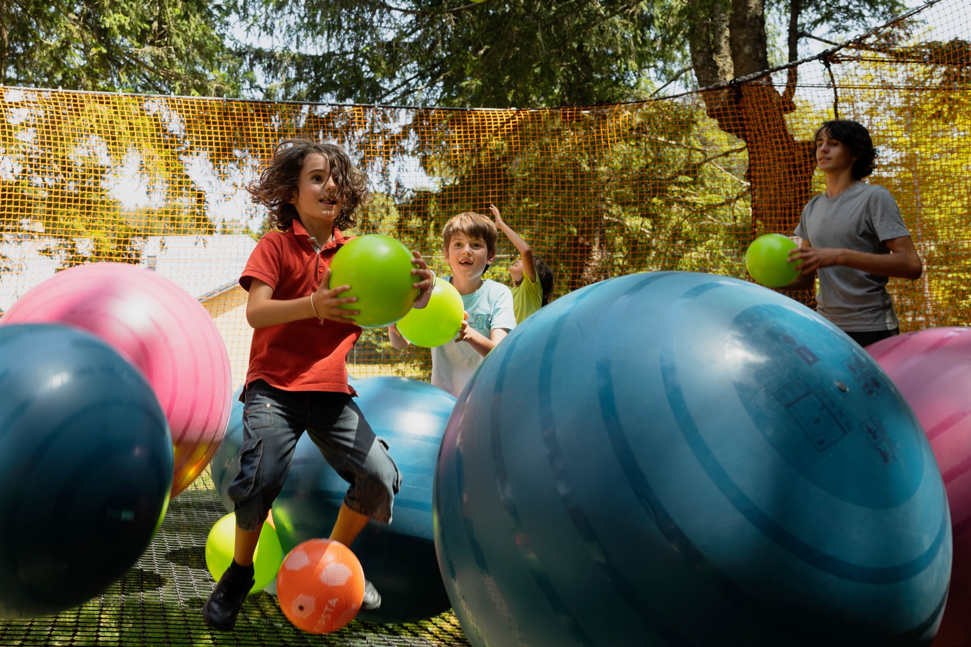 3 enfants, avec un ballon dans les mains, jouent au milieu de gros ballons.